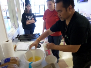 Freddy adds milk while Jerilynn and Marie watch during an APP French toast cooking class.