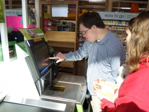 Aaron gets assistance from staff in operating a self-checkout machine.